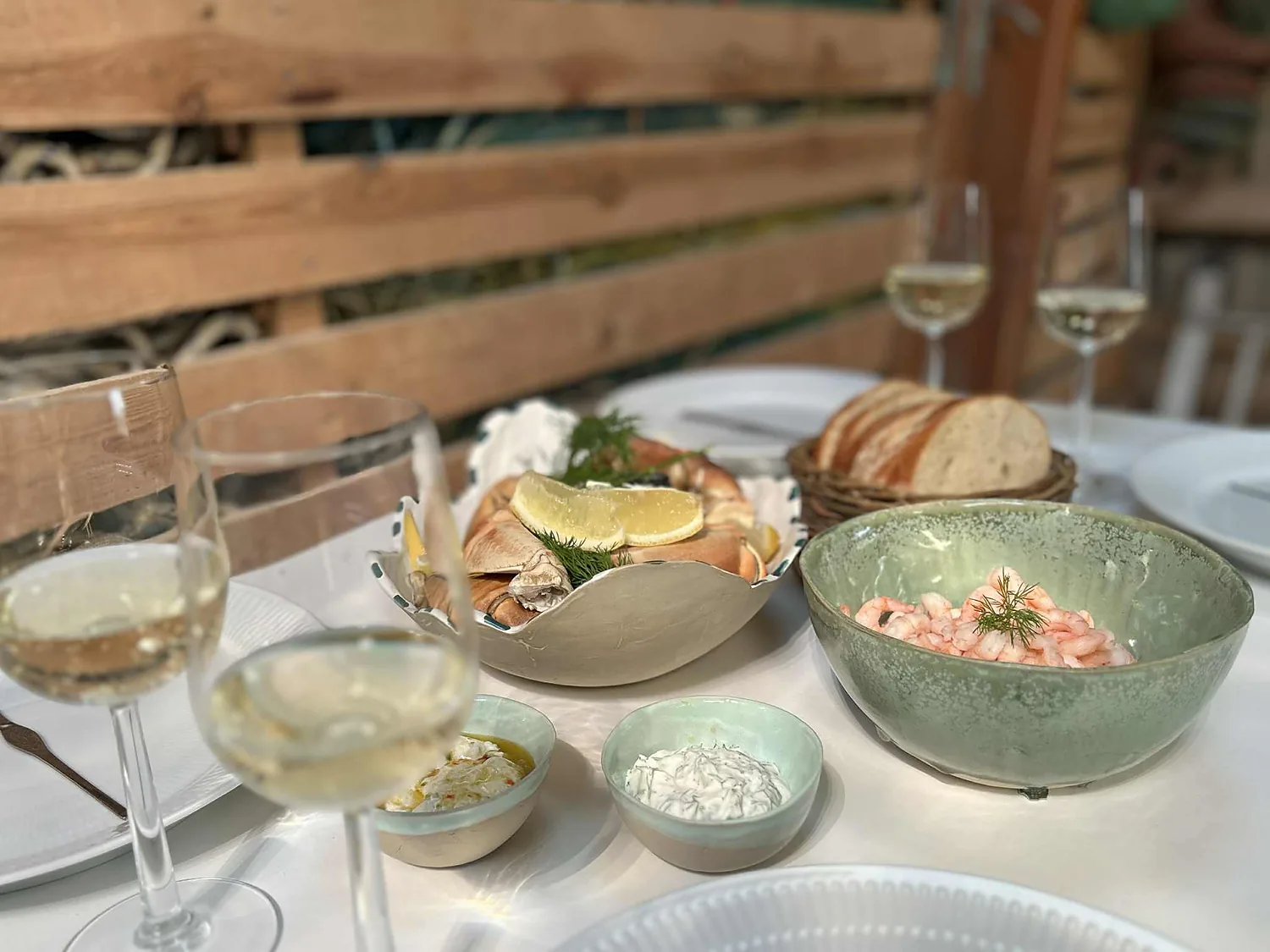 Dækket bord med hvidvinsglas, krabbekløer, rejer og brød.