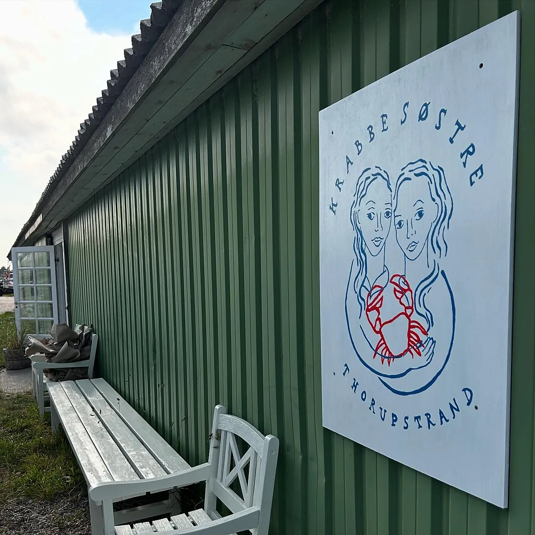 Krabbesøstres skilt på det grønne redskabsskur i Thorupstrand.